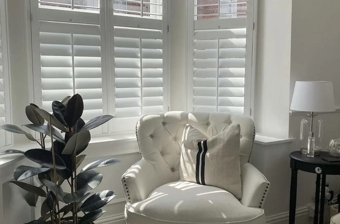 Splayed living room bay window wooden shutters with cream armchair