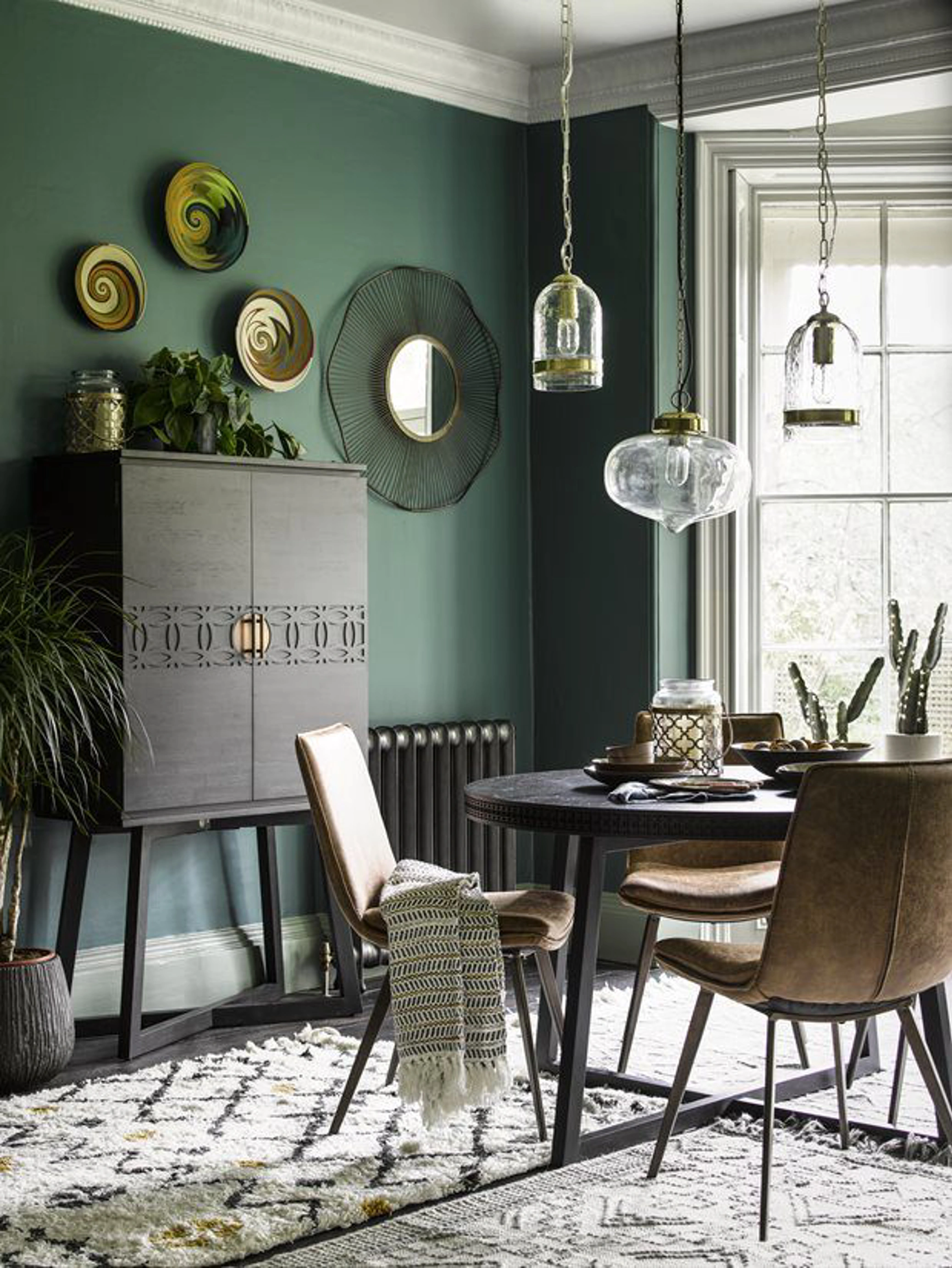 Green walls with black dining table and drinks cabinet 