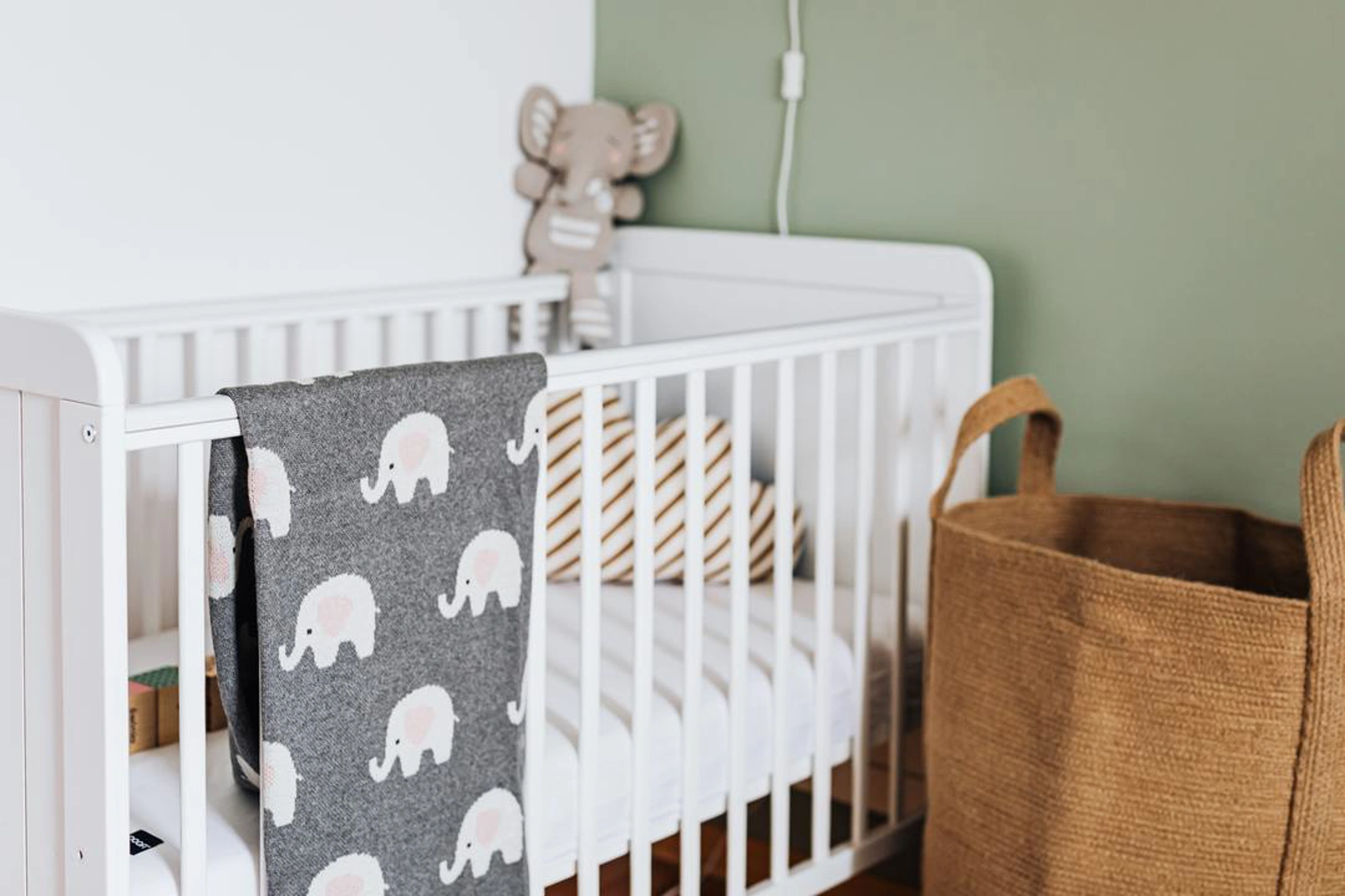 White cot with elephant print blanket in nursery