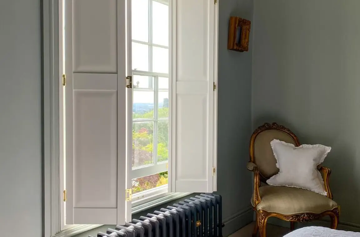 Vivid White solid raised wooden shutters and black radiator in bedroom