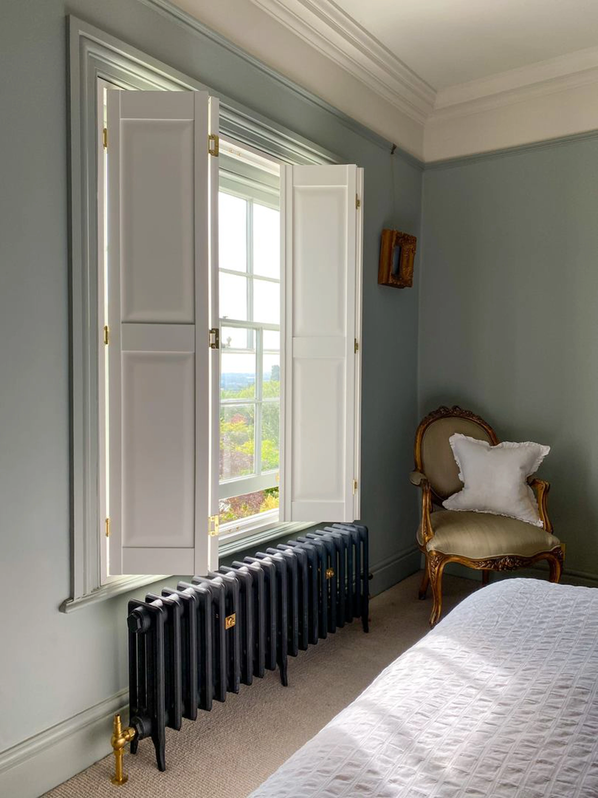 Vivid White solid raised wooden shutters and black radiator in bedroom